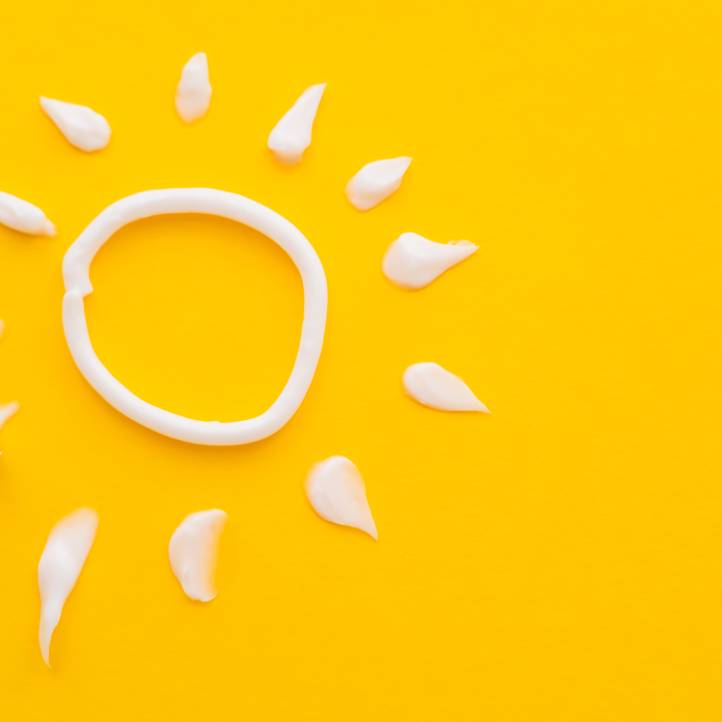 Dollops of white skin cream dispensed in the shape of a sun with rays, against a plain yellow surface.
