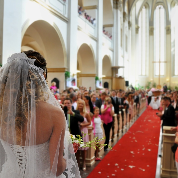 Bride and groom walking down the aisle toward the alter on their wedding day. The aisle is surrounded by guests.