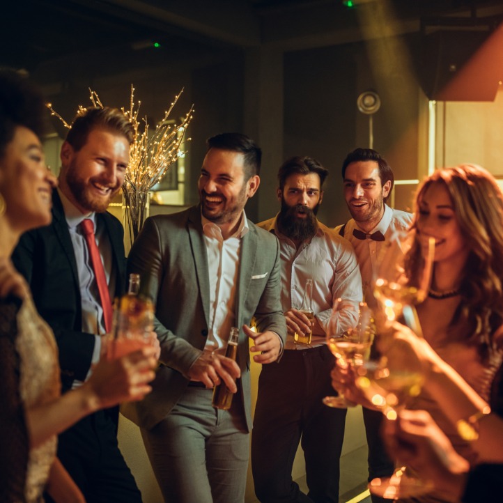 A group of well-dressed people standing in a semi-circle. They are all holding drink glasses and laughing.