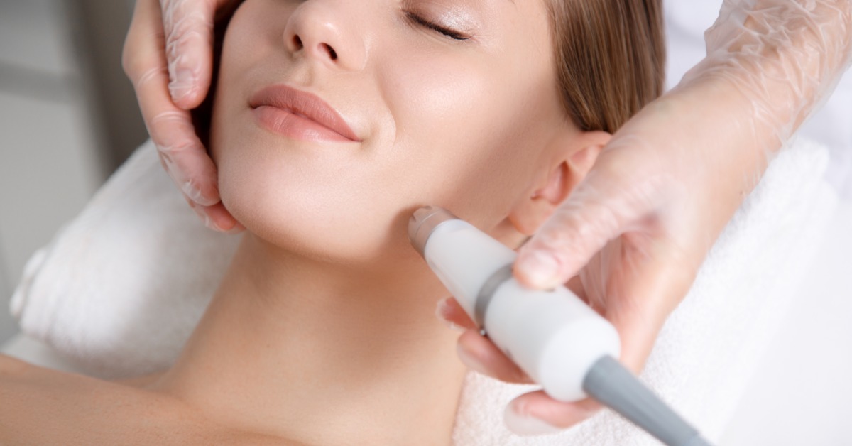 Woman rests with eyes closed as a gloved provider uses a skin rejuvenation device along her jawline.