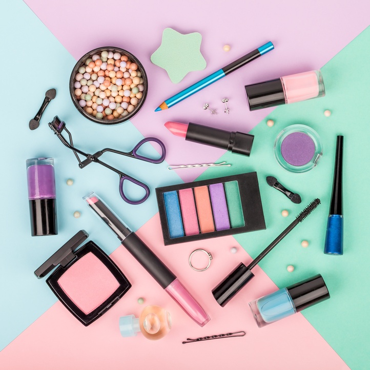 An assortment of makeup and cosmetic tools arranged on a background of pink, light blue, and mint green sections.